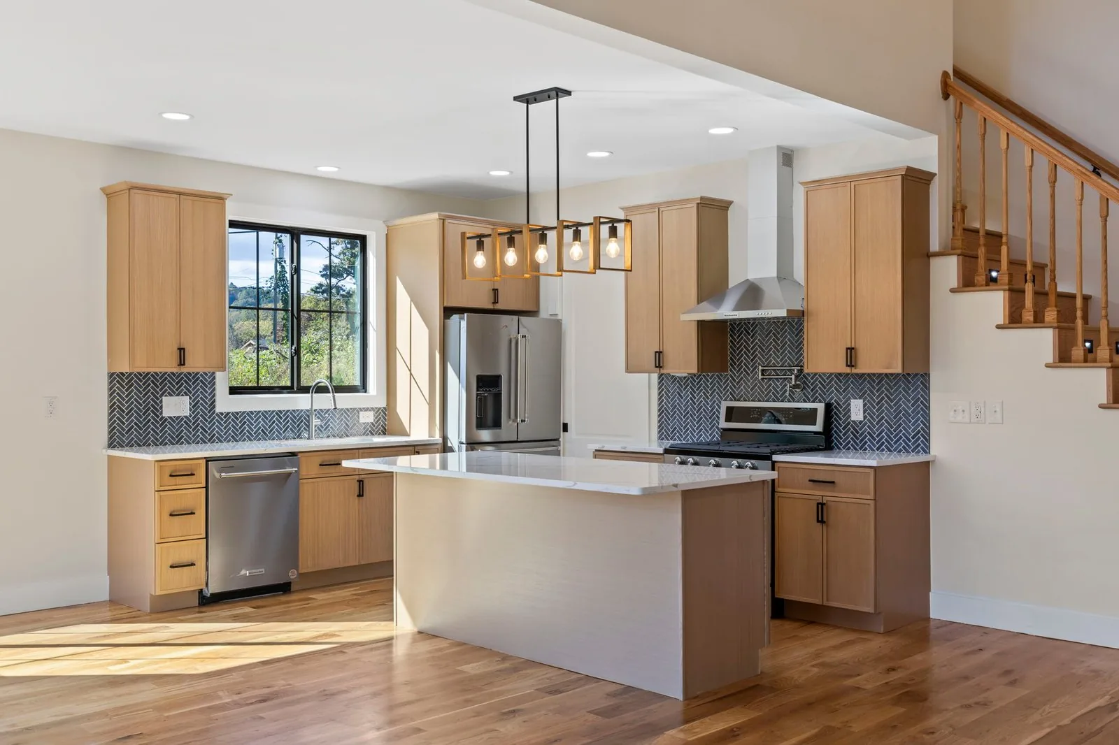 Open concept kitchen with white oak cabinets, quartz island and herringbone backsplash
