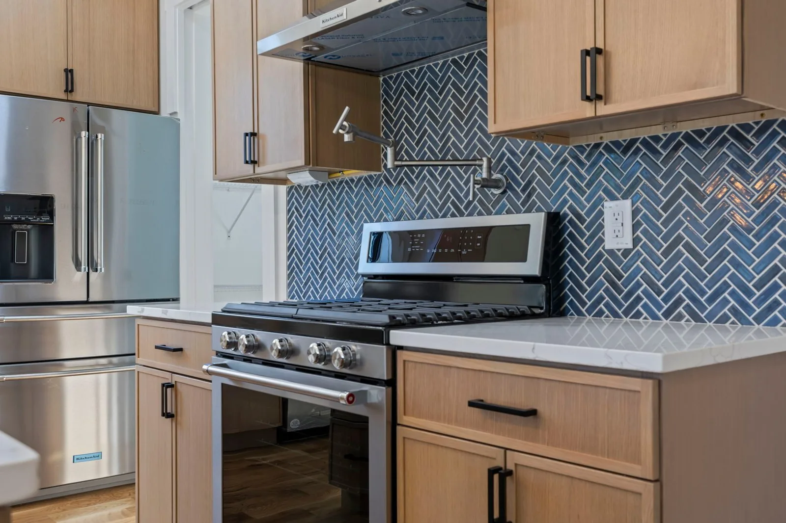 Kitchen detail with blue herringbone tile backsplash, gas range and pot filler