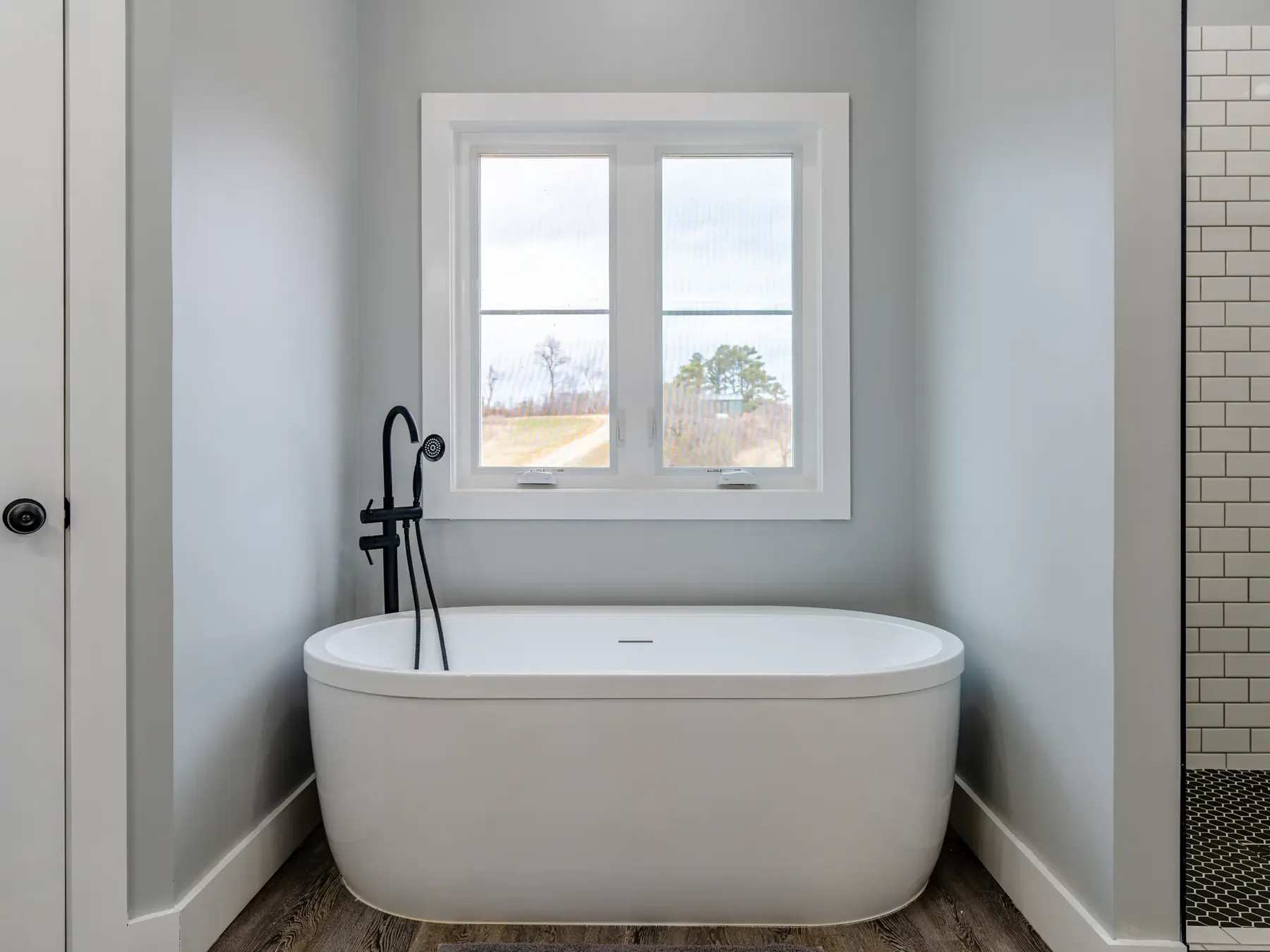 Freestanding soaking tub with matte black fixtures and a tile surround