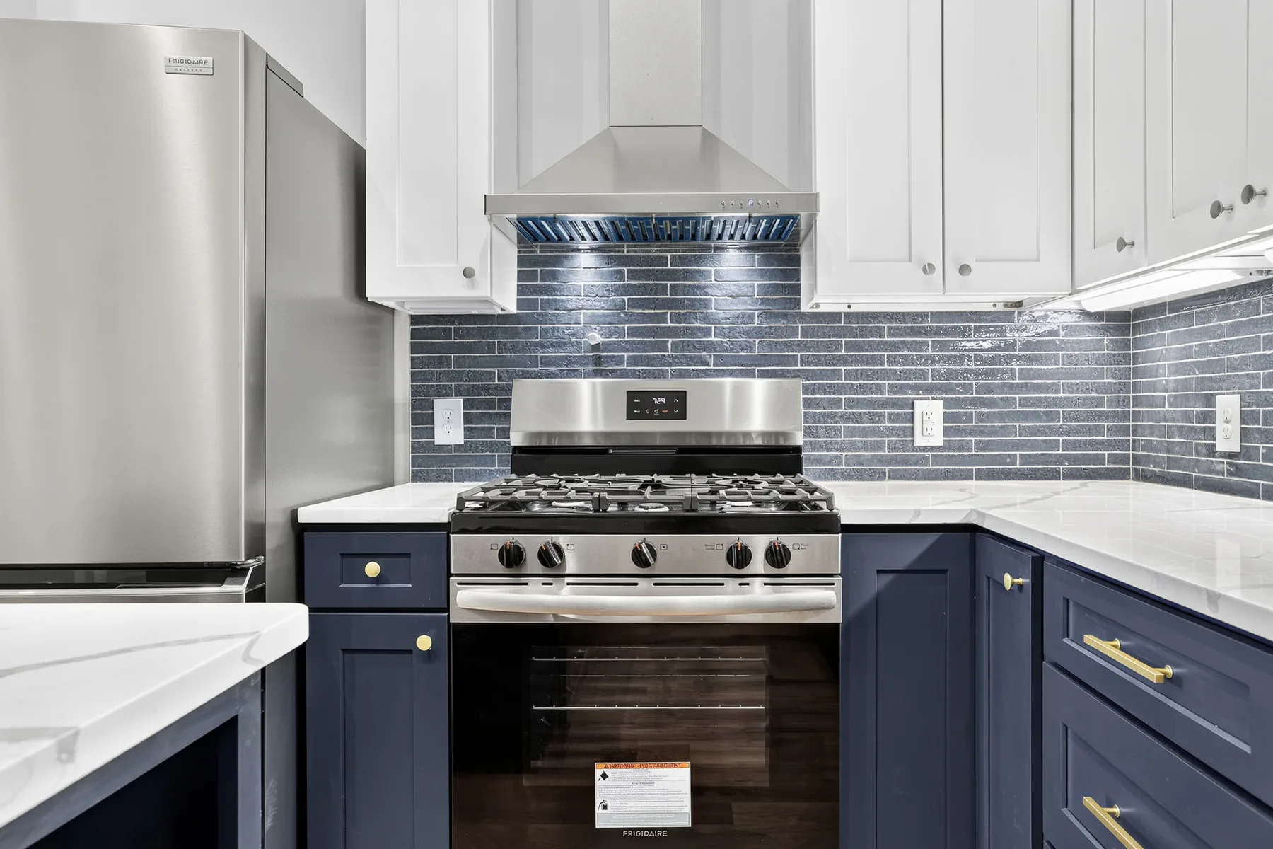Gas range with stainless hood and grey tile backsplash in a custom kitchen