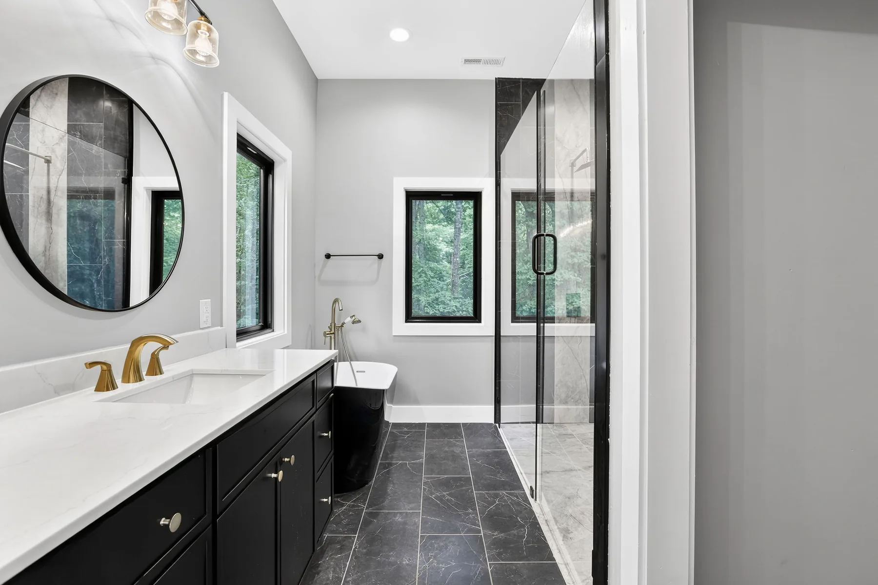 Bathroom vanity with round mirror, brass tap and a glass walk-in shower